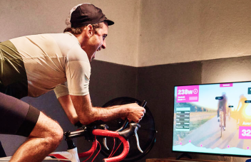 Ein Mann in Radlerkleidung sitzt auf einem Rennrad vor einem Fernseher